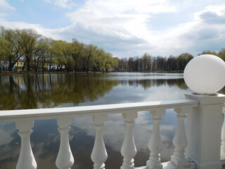 morning in the park with a lake, willow with young foliage and a beautiful white railing with decorative ball, springtime background
