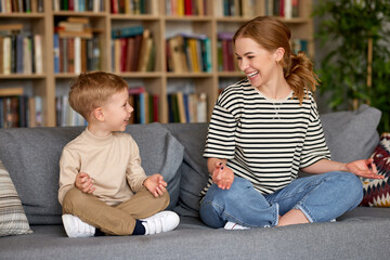 Mom and son sitting in lotus pose on sofa and meditating together