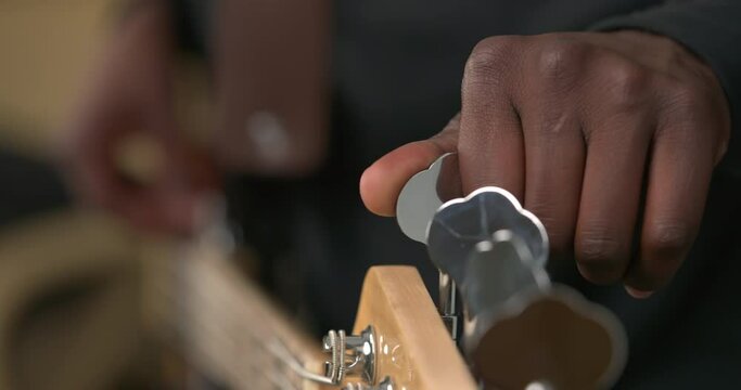 Close up of unrecognizable African man's hand tuning guitar. Guitarist checking and twisting pegs on guitar head while holding string instrument in hands. Blurred background