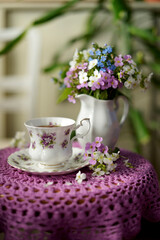 tea in a vintage china white cup and flowers on a lilac knitted napkin