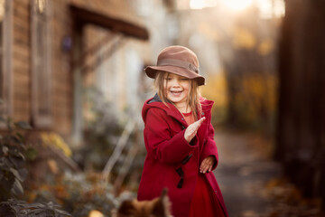 Cute funny caucasian child girl in red coat with dog in autumn street, children and animals