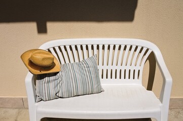 A cowboy wicker hat on a white bench with a striped vintage cushion in the garden (Marche, Italy,...