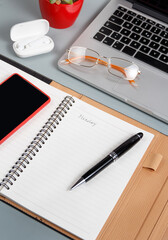 Laptop, cell phone and opened agenda on a grey desk close up.