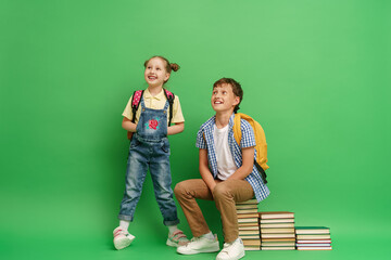 Two happy schoolchildren in loose clothes sit on stacks of school textbooks and reading books, and smile cheerfully against a green background. The concept of children's education. Back to school