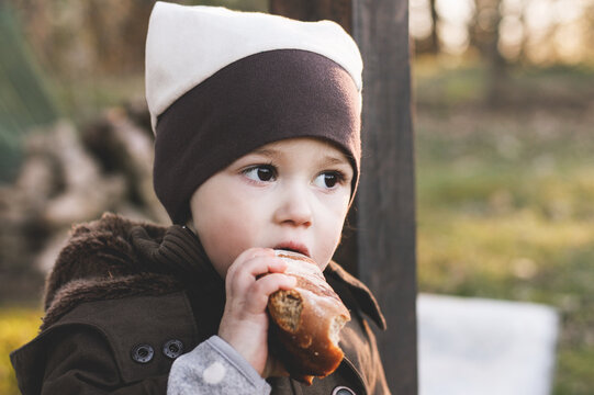 Little girl outsides in jacket and hat eating loaf of bread
