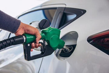 Man Handle pumping gasoline fuel nozzle to refuel. Vehicle fueling facility at petrol station. White car at gas station being filled with fuel. Transportation and ownership concept