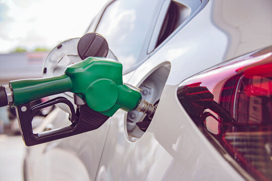Green Handle pumping gasoline fuel nozzle to refuel. Vehicle fueling facility at petrol station. White car at gas station being filled with fuel. Transportation and ownership concept