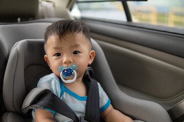 Local lifestyle Asian Chinese baby boy with emotion face and sucking pacifier while sit on child safety car seat