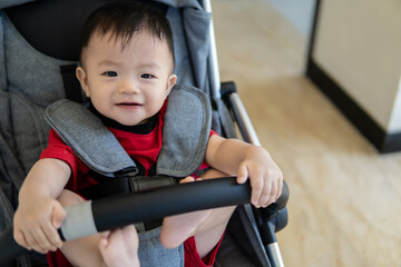 Happy and cute Asian Chinese baby boy sitting on stroller during short term holiday