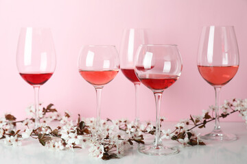 Glasses of wine and cherry flowers against pink background
