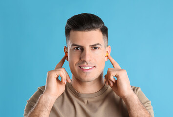 Man inserting foam ear plugs on light blue background