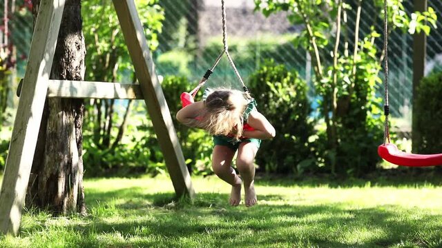 Happy little preschool girl having fun on swing in domestic garden. Healthy toddler child swinging on sunny summer day. Children activity outdoor, active smiling kid laughing