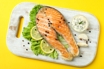 Concept of tasty eating with grilled salmon on yellow background