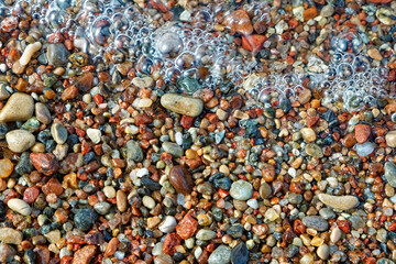 Multicoloured small sea pebbles and sea water foam