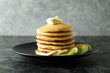 Plate with pancakes with butter, kiwi and banana on black smokey table