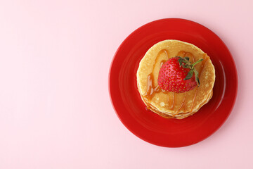 Plate with pancakes with strawberry and caramel on pink background