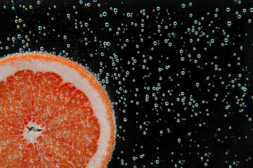 Slice of grapefruit in sparkling water on black background, closeup with space for text. Citrus soda