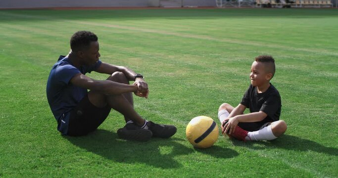 Diverse trainer and boy talking on football pitch