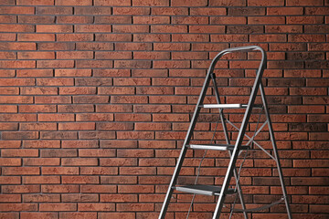 Modern metal stepladder against brick background. Space for text