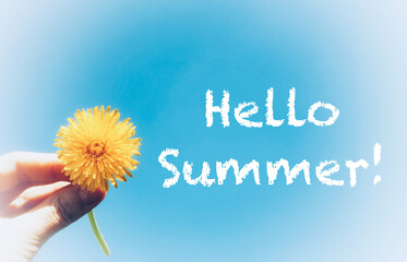 Bright yellow dandelion in a woman's hand against the background of blue sky. Summer wild flowers. Enjoying nature. Hello Summer. Banner with text