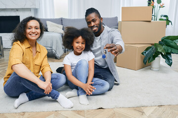 African American family moves into a new home. Father, mother, and daughter are happy sitting on a house floor after unpacking things. Buying or renting a house for a young family