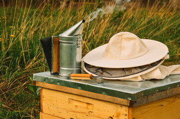 The beekeeper's tools are lying on the hive. Smoker, chisel and protective equipment of the beekeeper on the bee house. Apiary in nature. Honey production. Bees. Natural healthy honey.