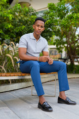 Obraz premium Full length shot of young African businessman outdoors sitting at park bench