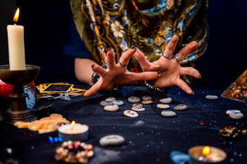 Female hands of a fortune teller read runes. Tarot cards, jewels and candles are on the table. The concept of divination, astrology and predicting the future