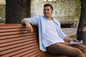 Fototapeta premium Happy man listening to audiobook on bench outdoors