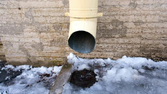 The bottom of a drainpipe with dripping snow melting