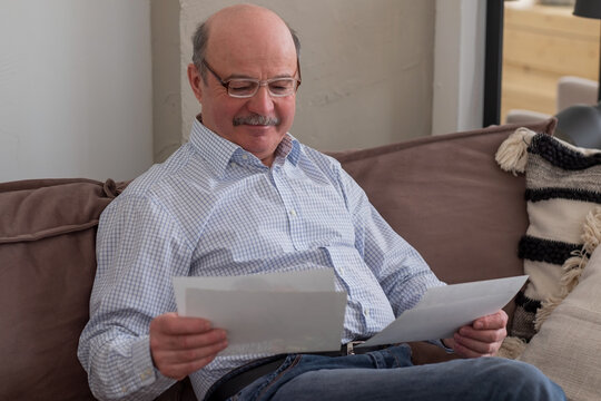 Senior man alone sitting on sofa at home holding photos thinking of memories