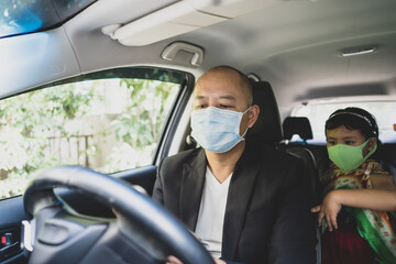 Father and daughter sitting in car wearing healthy face mask looking at smartphone.