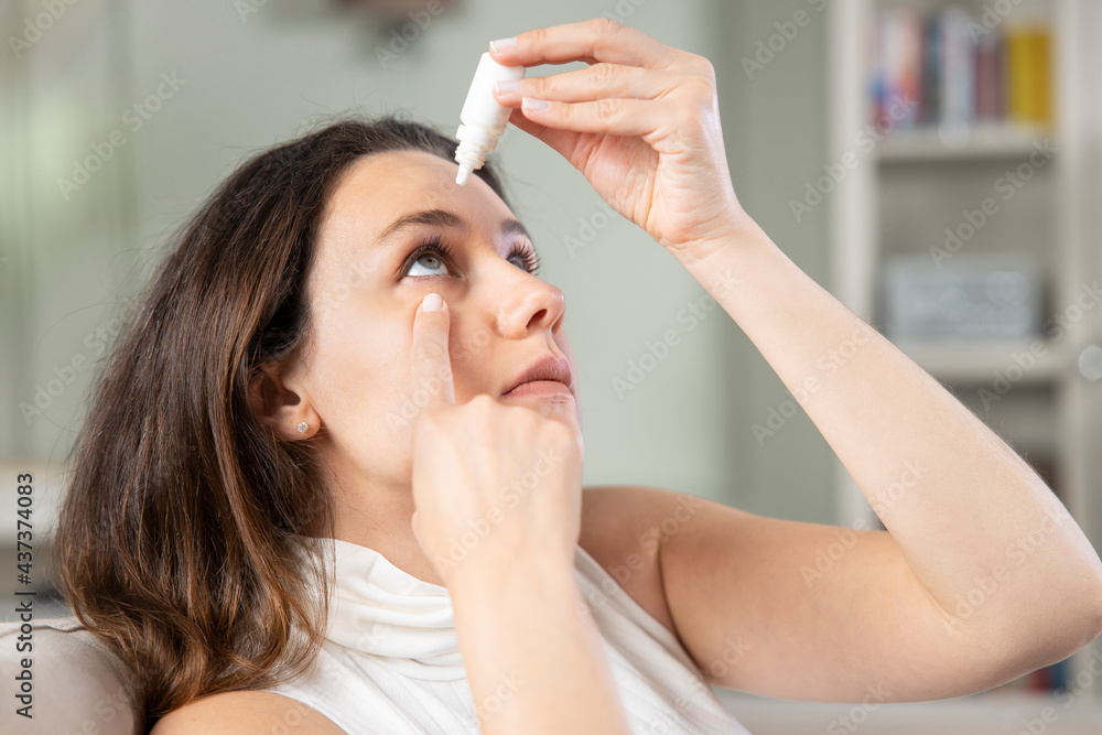 Wall mural young woman putting eye drops