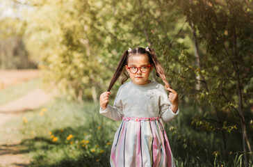 A cute little girl in glasses in nature on a sunny day