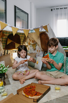 Children eating pizza and lemonade while camping at home in the living room