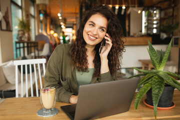 happy smiling Female freelancer talking on the phone, doing online shopping beautiful young girl working at a coffee shop with a laptop.