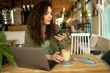Beautiful young girl working at a coffee shop with a laptop.female freelancer holding a phone connecting to internet via computer, doing online shopping