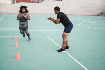 Plus size woman and personal trainer doing speed and agility cone drills workout session outdoor -...