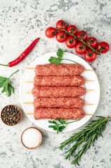 raw Lula kebab on skewers with spices on a white plate on a light stone background