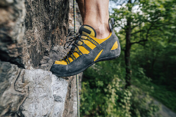 Close up view of a yellow climbing shoe on the rock. Climber's feet with orange and black climbing...