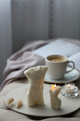 Fototapeta na wymiar Beautiful body shaped candles and cup of hot drink on bench indoors