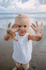 Cute little girl playing on tropical beach. Pretty child showing hands with dark sand and smiling....