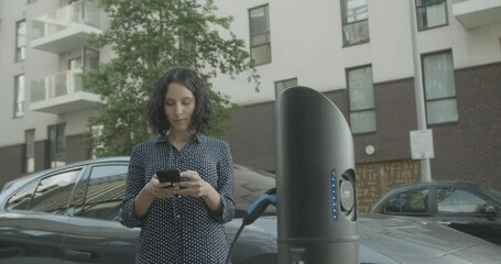 Hispanic female charging electric car at charging station in city