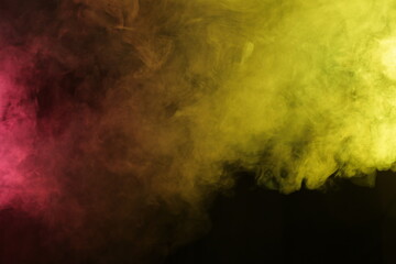 Artificial magic smoke in red-yellow light on black background