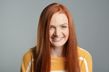 Fototapeta premium Candid portrait of happy young woman with charming smile and gorgeous red hair on grey background