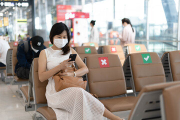 Asian women wear a mask and sit between chairs to reduce the spread of the coronavirus. Tourists wait to get on planes during the covid-19 outbreak.