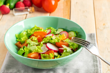 Recipe for vegetable salad with tomatoes, cucumbers and radishes. Seasonal dish on wooden background. Vegan food for diet.