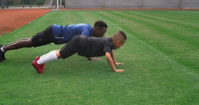 Diverse trainer and boy doing push ups on field
