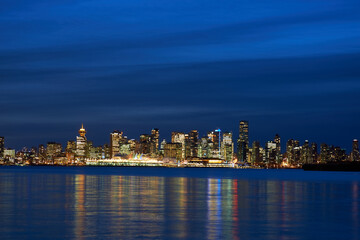 Fototapeta na wymiar Night city, panoramic scene of downtown reflected in blue water. Vancouver, Canada