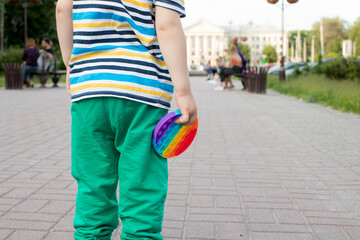 A small child holds a toy antistress pop it with a place for text in the background of the city park.